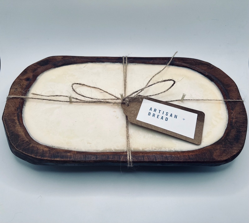 May include: A wooden bread bowl with a white interior, tied with twine and a brown paper tag that reads "Artisan Bread".