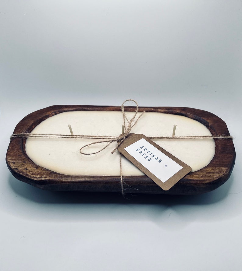 May include: A white candle in a wooden bread bowl with a brown paper tag that says "Artisan Bread".