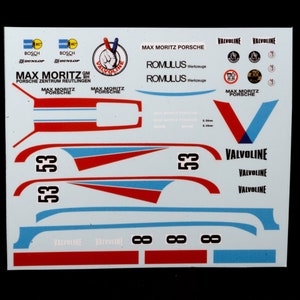 May include: A white sheet of decals for a model car. The decals include the words "Max Moritz Porsche", "Valvoline", "Romulus Werkzeuge", and "Porsche Zentrum Reutlingen". The decals are in red, blue, and black.