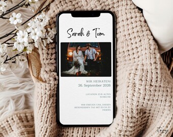 May include: A wedding announcement on a smartphone screen with a photo of a couple in front of a vintage van. The text reads "Sarah & Tom" and "Wir Heiraten! 26. September 2026. Location zur alten Scheune. Wir freuen uns, diesen besonderen Tag mit euch zu feiern."