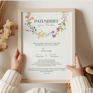 Könnte beinhalten: Ein gerahmter Druck mit dem Text "PATENBRIEF far Paula" und einem floralen Kranz. Der Druck enthält den Text "Mit der heutigen Taufe am 03. April 2026 übernimmst du die Patenschaft für Jonas" und Daten. Der Rahmen ist helles Holz.