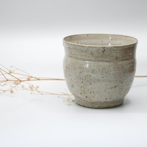 Peut inclure: Une tasse en céramique blanche avec un glaçage moucheté. La tasse a une forme arrondie et un bord légèrement évasé.