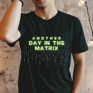 May include: A black t-shirt with a green graphic that reads "ANOTHER DAY IN THE MATRIX" in a pixelated font.