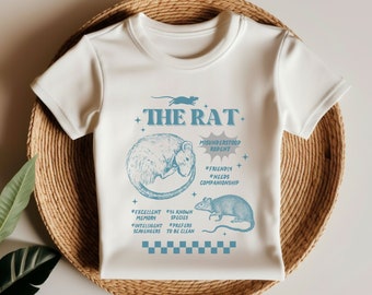 May include: White baby t-shirt with a blue graphic of a rat. The graphic includes the text "THE RAT", "MISUNDERSTOOD RODENT", "*FRIENDLY", "*NEEDS COMPANIONSHIP", "*EXCELLENT MEMORY", "#56 KNOWN SPECIES", "*INTELLIGENT SCAVENGERS", "*PREFERS TO BE CLEAN".
