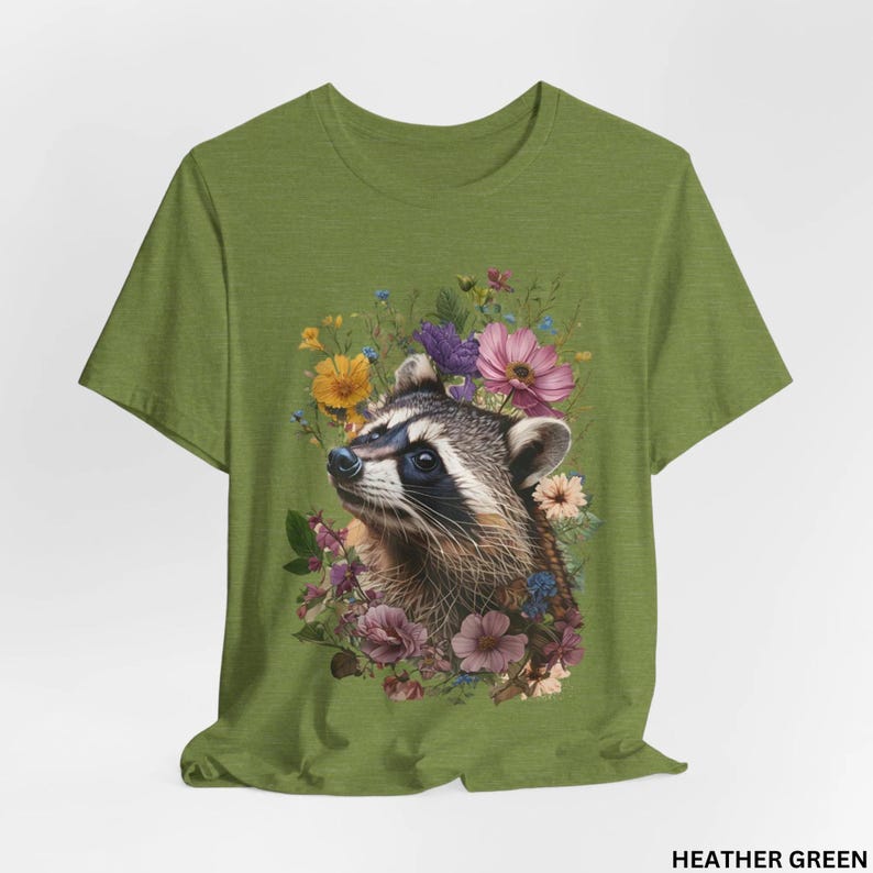 May include: A green t-shirt with a floral design featuring a raccoon with a white and black face. The flowers are pink, purple, yellow, and white.