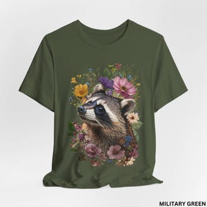 May include: A green t-shirt with a floral design featuring a raccoon's face. The raccoon is surrounded by pink, purple, yellow, and blue flowers.