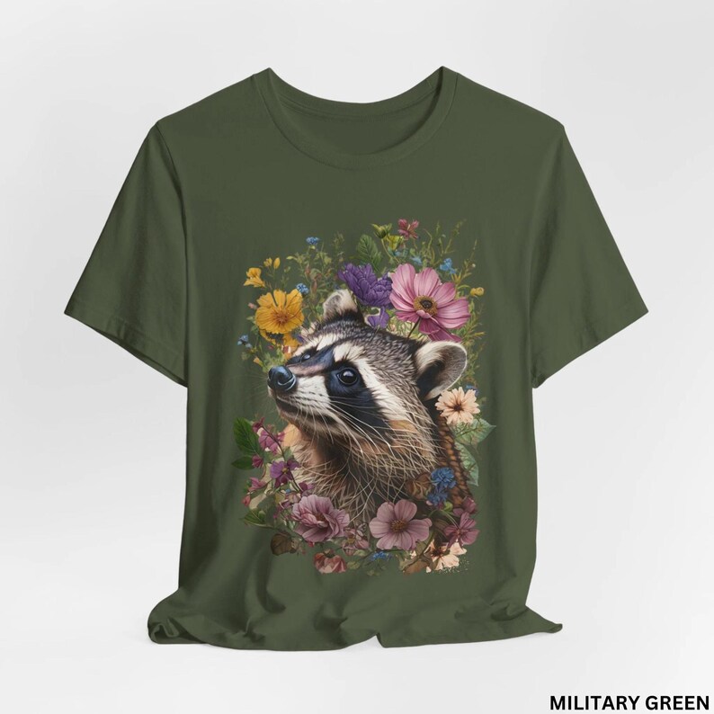 May include: A green t-shirt with a floral design featuring a raccoon's face. The raccoon is surrounded by pink, purple, yellow, and blue flowers.