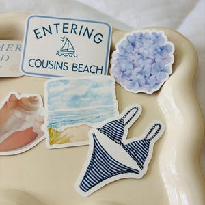 May include: A collection of stickers featuring a blue and white striped bikini, a sign that reads "Entering Cousins Beach", a watercolor beach scene, a blue hydrangea flower, and a seashell.