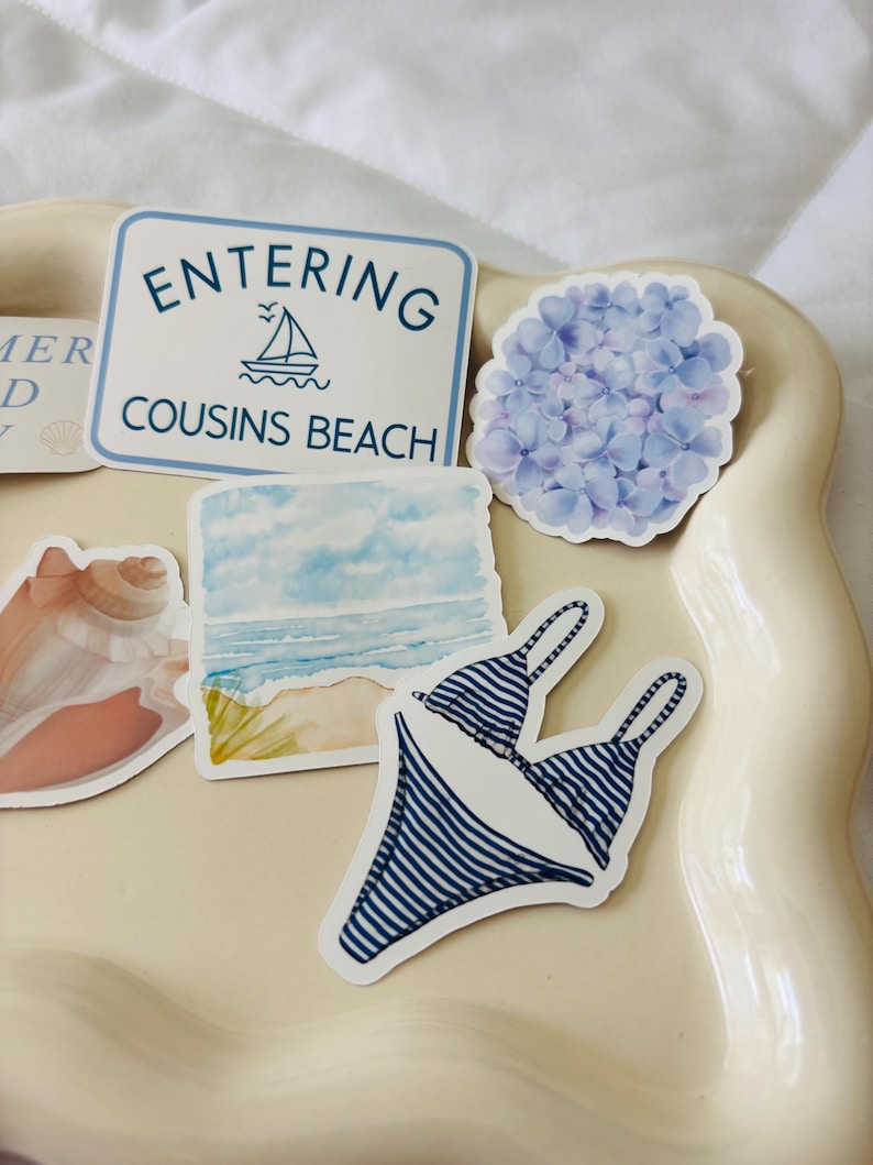 May include: A collection of stickers featuring a blue and white striped bikini, a sign that reads "Entering Cousins Beach", a watercolor beach scene, a blue hydrangea flower, and a seashell.
