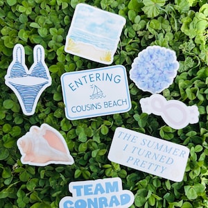 May include: A collection of stickers with a beach theme, including a blue and white striped bikini, a seashell, and a sign that says "Entering Cousins Beach." Other stickers include a beach scene, a hydrangea, and text that says "The Summer I Turned Pretty."