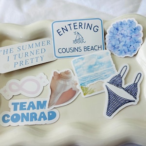 May include: A collection of stickers with a summer theme, including text that reads "The Summer I Turned Pretty", "Entering Cousins Beach", and "Team Conrad". Other stickers feature a seashell, a blue hydrangea, a bikini, and an infinity symbol.
