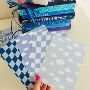 May include: Four blue and white patterned paper bookmarks with different designs. The designs include a checkered pattern, a cloud pattern, and a diamond pattern. The bookmarks are stacked on top of each other.