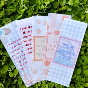 K&ouml;nnte beinhalten: F&uuml;nf dekorative Lesezeichen mit verschiedenen Designs und Texten. Ein Lesezeichen hat eine Segelboot-Illustration und Text. Ein anderes sagt "TEAM CONNIE BABY". Die anderen haben Pfirsich- und Blumenmuster.