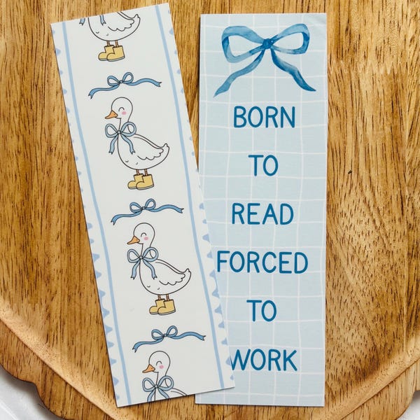Peut inclure: Deux marque-pages bleus et blancs. Un marque-page présente un motif répété d'un canard blanc portant des bottes jaunes et un nœud bleu. L'autre marque-page a un nœud bleu en haut et le texte "BORN TO READ FORCED TO WORK".