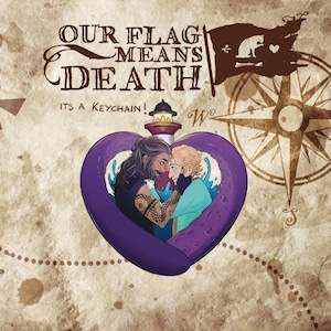 Puede incluir: Un llavero de corazón morado con un faro y dos figuras en su interior. El texto "Our Flag Means Death" está escrito encima del llavero. El texto "It's a Keychain!" está escrito debajo del llavero.