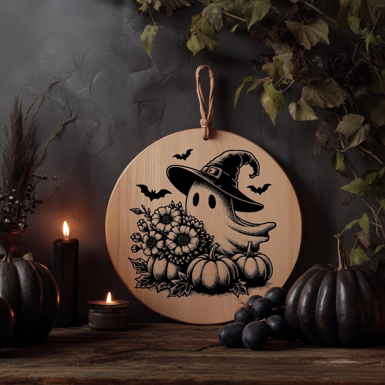 May include: A round wooden Halloween decoration featuring a ghost wearing a witch hat, surrounded by pumpkins, flowers, and bats. The design is in black and white, with a natural wood background and a jute rope for hanging.