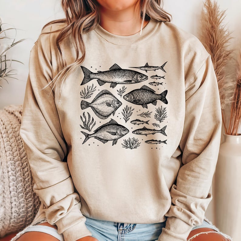 Może przedstawiać: Beżowa bluza z czarnym nadrukiem graficznym przedstawiającym r&oacute;żne ryby i wodorosty. Ryby są narysowane w stylu vintage.