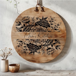 May include: Round wooden sign with a black floral design and the text "Mom's Kitchen".
