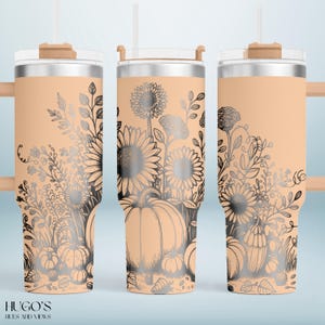 May include: A stainless steel tumbler with a peach-colored base and a floral design featuring sunflowers and pumpkins. The design is in black and silver. The tumbler has a clear lid and a straw. The text "HUGO'S HUES AND VIEWS" is at the bottom.