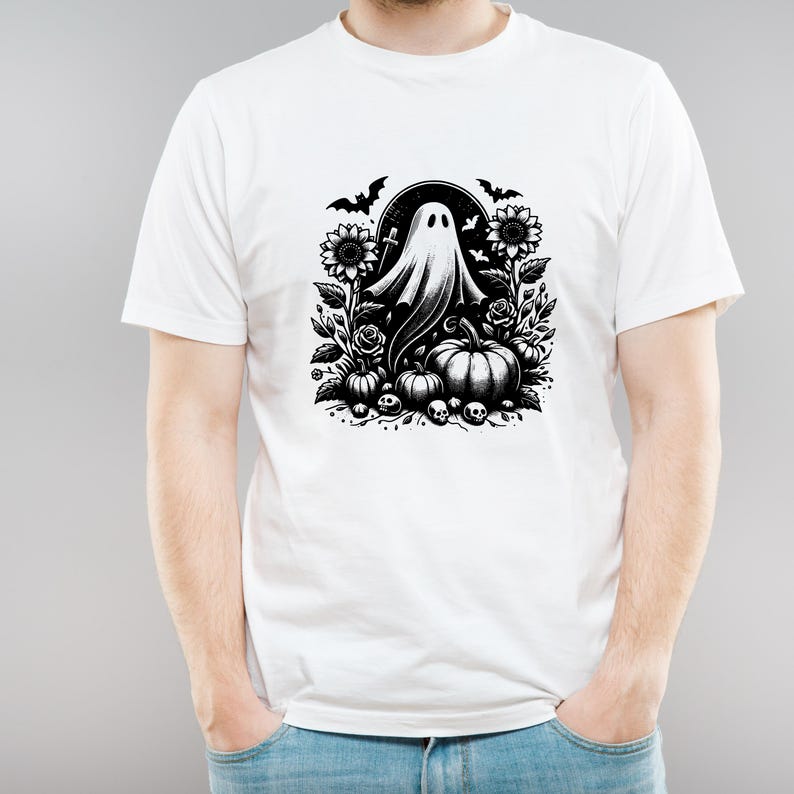 May include: White t-shirt featuring a black and white Halloween design. The graphic includes a ghost, pumpkins, sunflowers, roses, bats, and skulls. The design is centered on the front of the shirt.