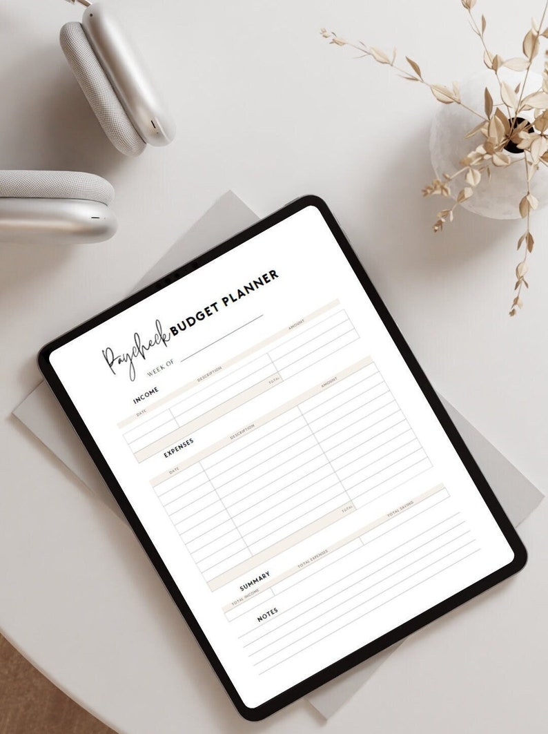 May include: A digital paycheck budget planner on a tablet. The planner has sections for income, expenses, summary, and notes. The text "Paycheck Budget Planner" is at the top in a handwritten font. The tablet is on a white surface.
