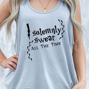 May include: A light blue sleeveless tank top featuring black text that reads "I solemnly swear all the time" with a lightning bolt graphic and a trail of small footprints surrounding the words in a decorative, stylized font.