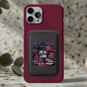 May include: A deep burgundy smartphone case with a black magnetic card holder attached to the back. The holder features a graphic of stacks of books, pink roses, and a gothic archway with the text "GOOD GIRLS READ BAD BOOKS" in white lettering.