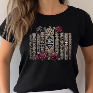 May include: A black t-shirt featuring a graphic of a row of ornate, vintage-style books with gold detailing. The central book spine displays the text 'I PREFER THE VILLAIN'. The design is decorated with deep red and black roses and a small skull.