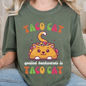 Funny taco cat palindrome shirt displayed on moss green Comfort Colors tee featuring bright colorful typography and adorable taco cat character graphic.
