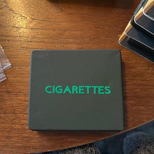以下が含まれることがあります： 緑色の文字で「CIGARETTES」と書かれた濃い緑色の箱