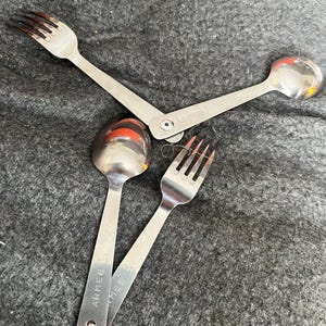 Könnte beinhalten: Ein Set aus drei silbernen Besteckteilen, eine Gabel und zwei Löffel, mit der Gravur "ARMEE" auf einem der Löffel.