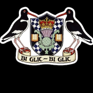 Puede incluir: Un escudo negro y blanco con una corona, un cardo y dos pájaros negros y blancos. El escudo está rodeado de un rollo blanco con el texto "BI GLIC - BI GLIC".