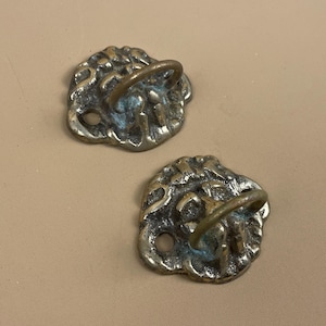 May include: Two ornate brass hooks with a decorative design and a ring for hanging items.