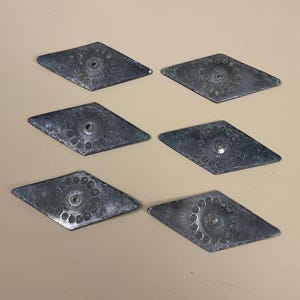 May include: Six diamond-shaped metal decorative pieces. Each has a central hole encircled by a pattern of small dots. The metal has a weathered, aged look, with a slightly tarnished silver colour.
