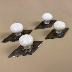 May include: Four cabinet knobs. Each has a white, cracked ceramic sphere on a diamond-shaped, dark metal base. The metal bases have a hammered texture and a border of small, evenly spaced circles.