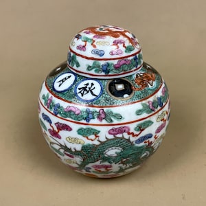 May include: A white ceramic ginger jar with a lid, decorated with a dragon design. The jar features floral and cloud patterns, and the lid has a red and orange design. The jar has the Chinese character for "Autumn".