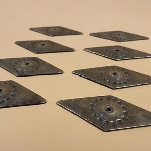May include: Eight diamond-shaped metal pieces are displayed. Each has a central hole and a circular pattern of indentations. The metal has a dark, aged appearance, suggesting an antique finish.