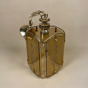 May include: A gold-toned pendant light fixture with a geometric, square-shaped design. The fixture has four amber glass panels with etched floral patterns. The light fixture is suspended from a chain.