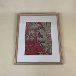 Pode incluir: Um peda&ccedil;o de tecido vermelho e branco estampado emoldurado com uma borda preta. O tecido est&aacute; em uma moldura de madeira com um passe-partout branco.