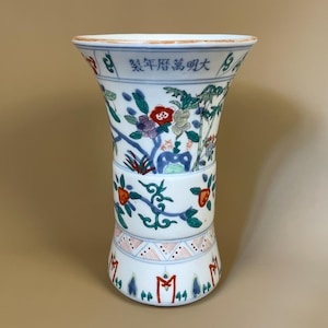 May include: A white porcelain vase with a flared top and a bulbous midsection. The vase is decorated with colourful floral and foliage patterns in red, blue, green, and purple. The rim has a red border, and there is text in Chinese characters.