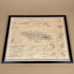 May include: A framed vintage map of the British West Indies, showing detailed illustrations of the islands. The map is in a black frame, with the title "The British Islands West Indies" at the top. The map is printed in black and white.