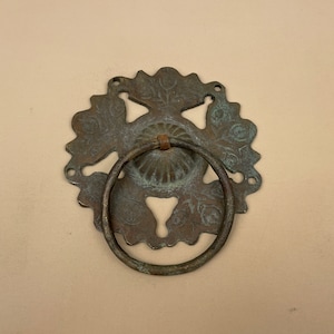 May include: A circular, ornate, brass door knocker with a ring handle. The knocker has a floral design and a patina finish.