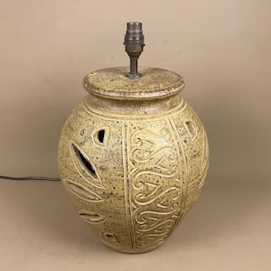 May include: A ceramic table lamp with a beige and brown speckled finish. The lamp features cut-out leaf shapes and a decorative pattern. The lamp has a metal lamp holder and a power cord.