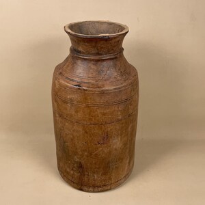 May include: A tall, brown wooden vase with a rounded body and a slightly flared top. The vase has a smooth, polished finish and is decorated with horizontal lines.