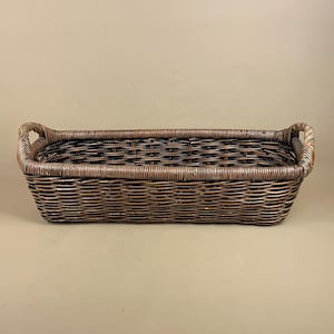 May include: A rectangular wicker basket with two handles. The basket is woven in shades of brown and dark brown. The handles are a lighter brown. The basket is empty and rests on a neutral background.