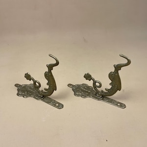 May include: Two ornate metal hooks in the shape of a dragon with a decorative base. The hooks are gold in colour.