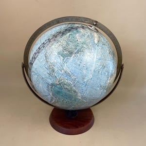 May include: A vintage globe featuring a light blue and white map, held within a metal meridian ring. It is mounted on a dark wooden base. The globe displays continents and oceans.