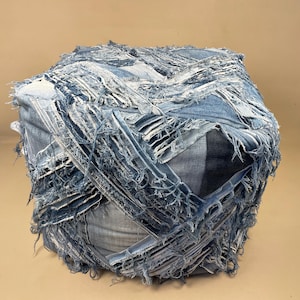 May include: A blue denim ottoman with a patchwork design. The ottoman is made of multiple pieces of denim fabric that have been sewn together and frayed at the edges.