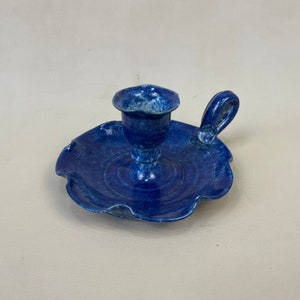 May include: Blue ceramic candle holder with a scalloped base and a handle. The holder has a speckled blue glaze.