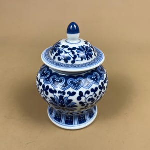 May include: A blue and white ceramic jar with a lid. The jar has a floral pattern in blue on a white base. The lid has a small blue knob. The jar is a decorative item, suitable for display.